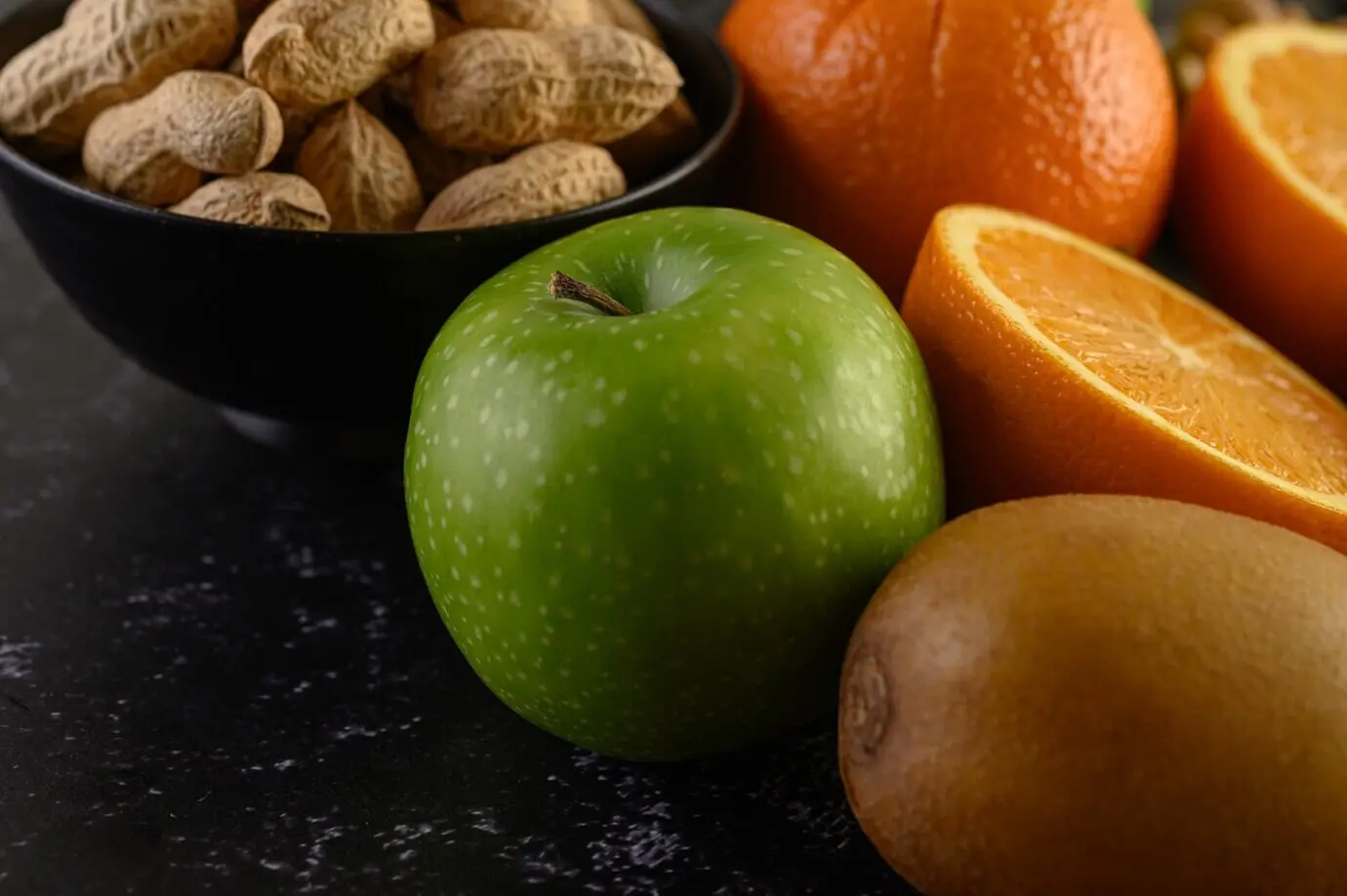 A close-up of an apple, a peanut, a slice of fresh orange, kiwi, and avocado.
